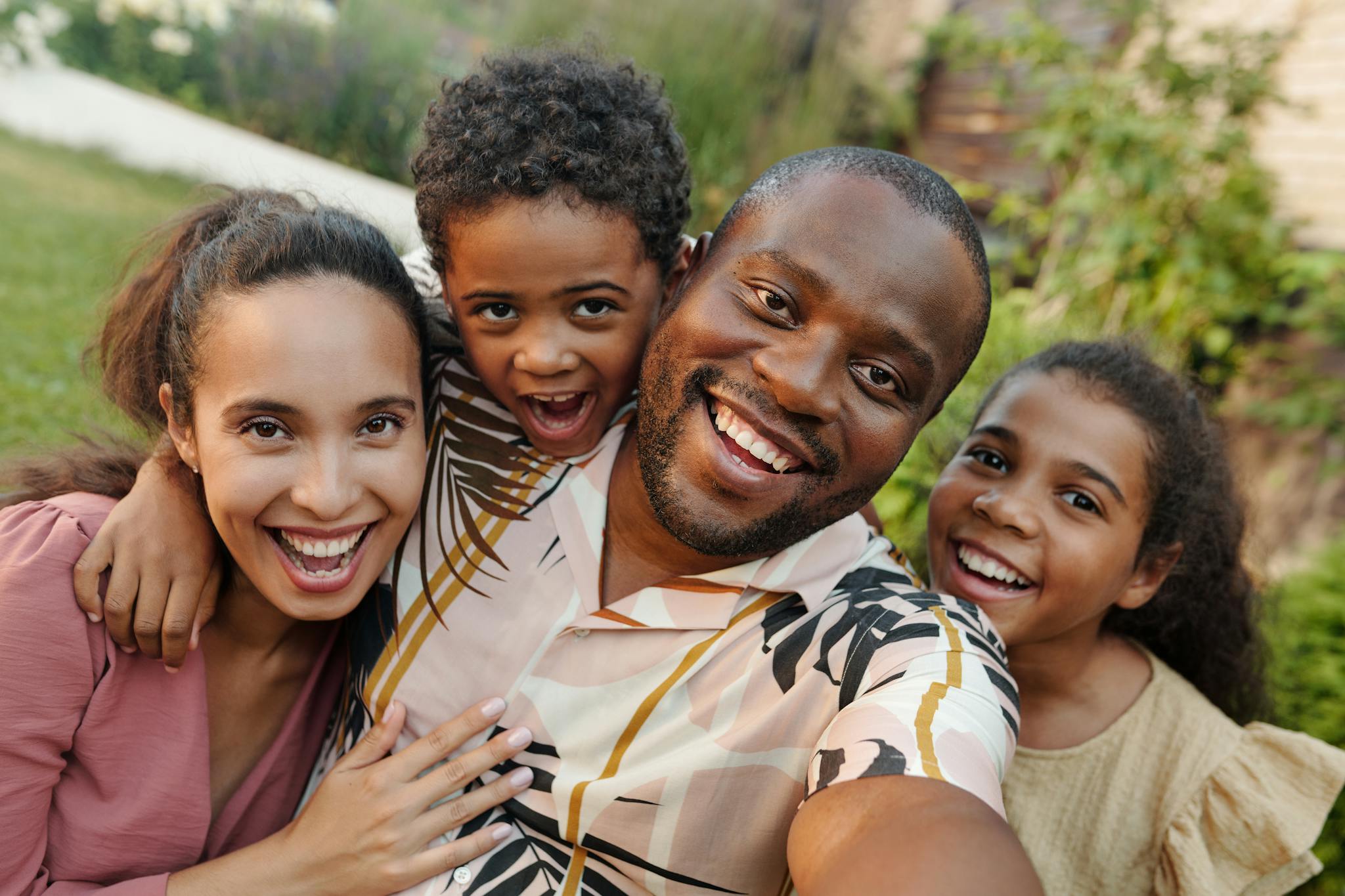 A joyful multicultural family taking a selfie outdoors in a lush garden setting.