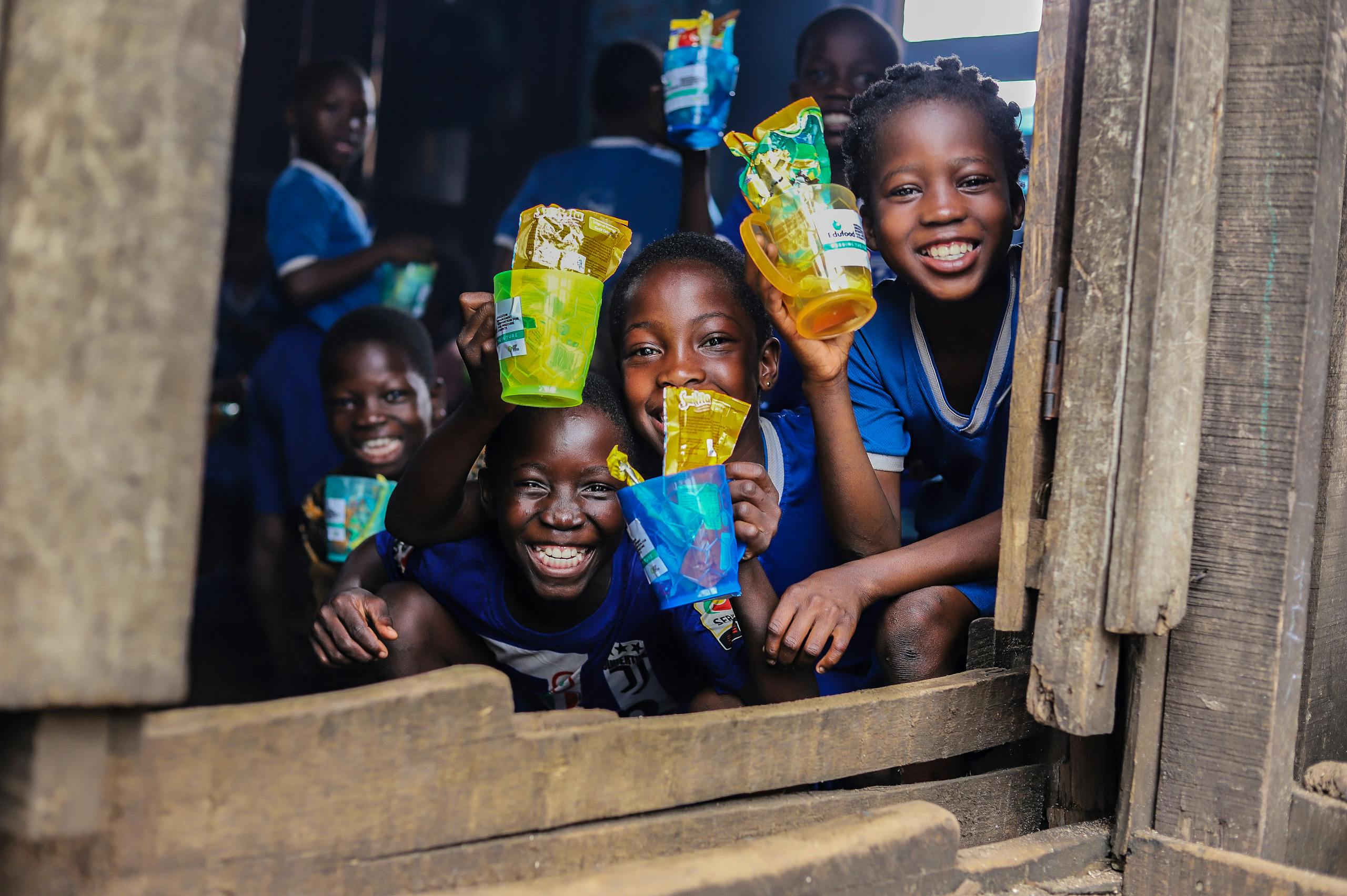 Children smiling and holding colorful recycled plastic cups in a school setting.