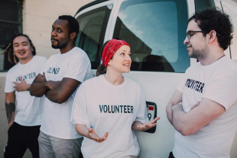 Four volunteers interacting by a van, promoting community service and involvement.